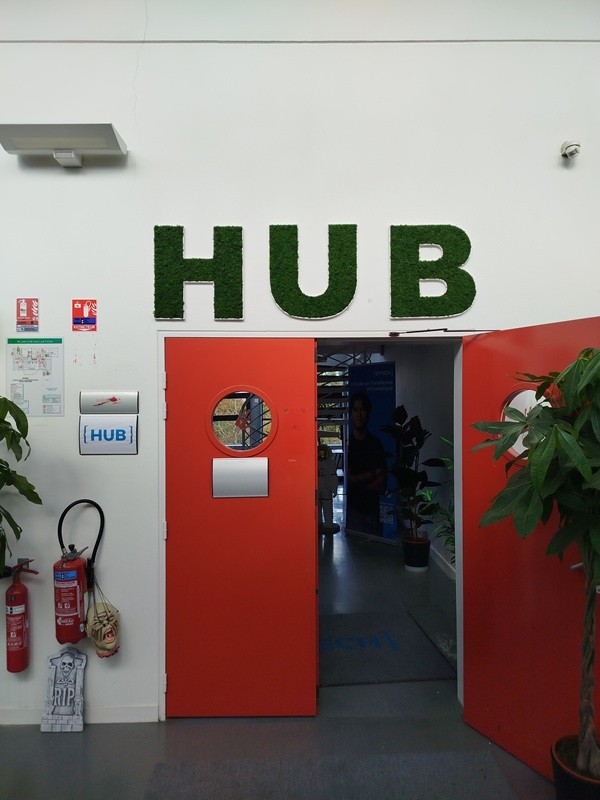 Lettres végétales stabilisées formant le mot HUB installées au-dessus d’une porte rouge dans un espace professionnel à Rennes.